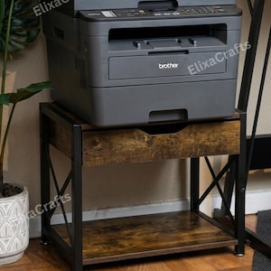 May include: A dark gray Brother multifunction printer sits atop a rectangular printer stand. The stand features a black metal frame with X-shaped side supports, a single drawer with a rustic brown wood-grain finish, and an open bottom shelf.