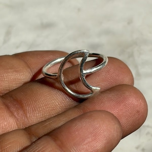 Puede incluir: Un anillo plateado con un diseño de media luna. El anillo está hecho de una banda delgada con una forma de luna recortada. El anillo se muestra en la mano de una persona.