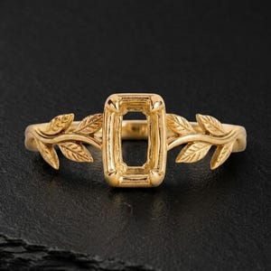 Peut inclure: Une bague en or dotée d'un sertissage rectangulaire central à griffes conçu pour accueillir une pierre précieuse. L'anneau est orné d'un relief détaillé de feuilles et de vignes s'étendant de chaque côté du sertissage central.