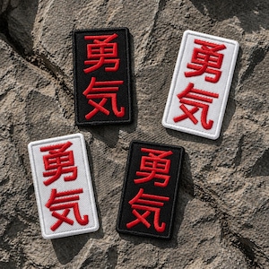 May include: Four rectangular embroidered patches with Japanese characters in red. Two patches have a black background, and two have a white background. The patches are arranged on a textured, gray surface.