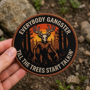 May include: A circular embroidered patch featuring a central creature with a deer skull head and antlers, set against a forest and orange sunset background. The text "EVERYBODY GANGSTER TILL THE TREES START TALKIN'" is stitched in white along the border.