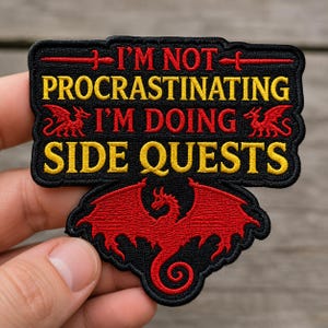 May include: A black embroidered patch featuring the red and yellow text I'M NOT PROCRASTINATING I'M DOING SIDE QUESTS. The design includes a large red dragon at the bottom, two smaller red dragons on the sides, and a red sword icon above the text.