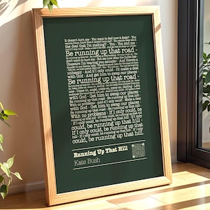 Pode incluir: Uma impressão emoldurada com a letra da música "Running Up That Hill" de Kate Bush em um fundo verde escuro. O texto é branco e a moldura é de madeira clara. A impressão está encostada em uma parede perto de uma janela.