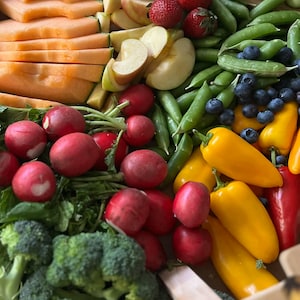 Könnte beinhalten: Eine bunte Auswahl an frischem Obst und Gemüse, arrangiert auf einem Holzbrett. Das Bild zeigt geschnittene Cantaloupe, Apfelscheiben, Erdbeeren, Zuckerschoten, Blaubeeren, Radieschen, gelbe und rote Paprika und Brokkoli.
