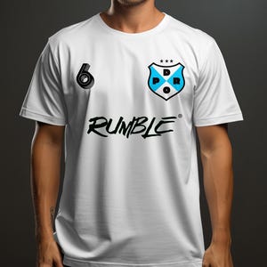 Pode incluir: Camiseta branca com gráficos em preto e azul claro. Apresenta um logotipo de escudo com "DPR" e estrelas, um gráfico com o número "6" e a palavra "RUMBLE" em uma fonte estilizada. A camiseta é de manga curta.
