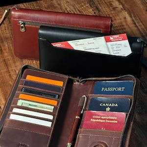 May include: A collection of leather travel accessories, including a burgundy zippered clutch, a black wallet with a boarding pass, and a brown passport holder. The passport holder contains a pen, cards, cash, and passports. The boarding pass is for a flight to Moscow.