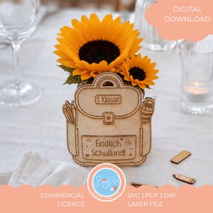 May include: A wooden school bag-shaped flower holder with sunflowers. The holder has the text "1. Klasse" and "Endlich Schulkind!". The design includes pencil and school cone illustrations. The image also includes a pencil and ruler-shaped wooden cutouts.