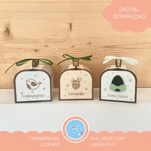 Könnte beinhalten: Drei dekorative Holzkisten mit gewölbten Deckeln, jede mit einem anderen Design und Text. Die Kisten haben ein hellbraunes und weißes Farbschema mit grünen oder weißen Schleifenhenkeln. Der Text enthält "Frühlingsgrüße", "Ostergrüße" und "Frohe Ostern".