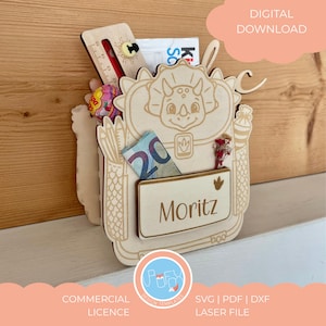Puede incluir: Organizador de madera cortado con láser con forma de dinosaurio, con el nombre "Moritz". Contiene una regla, caramelos y un billete de 20 euros. El diseño incluye el texto "DESCARGA DIGITAL".