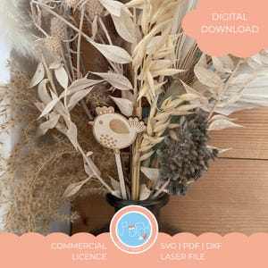 Puede incluir: Un elemento decorativo de madera con forma de pájaro sobre un palito, colocado en un jarrón con flores y hierbas secas. La imagen incluye el texto "DESCARGA DIGITAL", "LICENCIA COMERCIAL" y "SVG | PDF | DXF ARCHIVO LÁSER".