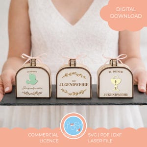 Puede incluir: Tres cajas de regalo de madera con tapas arqueadas, cada una con un diseño diferente: una paloma, texto y un cáliz. Las cajas están atadas con cintas rosas y están etiquetadas con texto alemán. El texto "Digital Download" está en la esquina superior derecha.