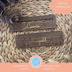 Puede incluir: Tres reglas de madera con marcas grabadas y elementos decorativos. Dos reglas presentan nombres dorados, "Leonie" y "Leopold". Las reglas están adornadas con ilustraciones temáticas escolares. La imagen también incluye el texto "DESCARGA DIGITAL" y "LICENCIA COMERCIAL."
