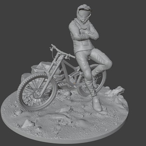 May include: A gray 3D-printed figurine of a person in a racing suit and helmet, leaning against a mountain bike. The figure is posed on a rocky terrain base, with the bike's details clearly visible.