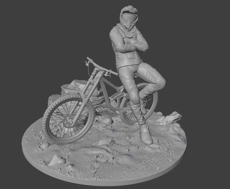 May include: A gray 3D-printed figurine of a person in a racing suit and helmet, leaning against a mountain bike. The figure is posed on a rocky terrain base, with the bike's details clearly visible.