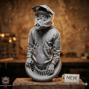 May include: A gray sculpture of a figure wearing a motorcycle helmet and hoodie, with skeletal hands holding a tire. The sculpture is displayed on a wooden surface. A tag reads "NEW".