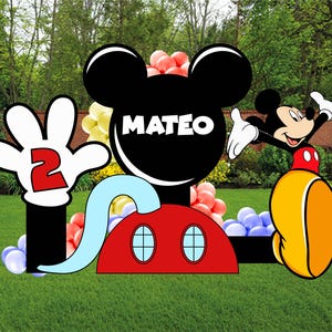 Op de afbeelding: Een grote feestuitsparing met Mickey Mouse-thema, voorzien van een zwart silhouet van een hoofd met de naam MATEO in witte letters, een rode basis met twee blauwe ovale accenten, een witte gehandschoende hand met een rood cijfer 2 en Mickey.