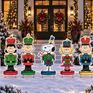 May include: A set of five Peanuts character yard decorations featuring Lucy, Charlie Brown, Snoopy with Woodstock, Sally, and Linus dressed as toy soldiers. Each figure stands on a circular base and measures 36 inches tall, displaying vibrant holiday colors and festive uniforms.