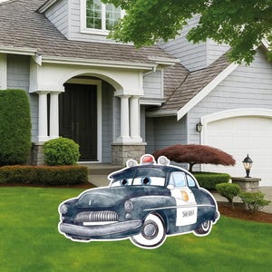 May include: A watercolor-style yard sign featuring a dark blue vintage police car with large blue eyes on the windshield, a red siren on the roof, and the word SHERIFF printed in black on the white door panel, displayed on a green lawn.