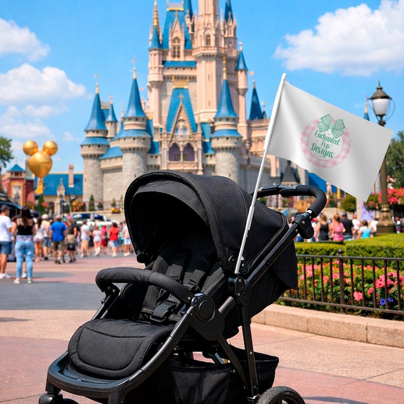 Puede incluir: Un cochecito negro con una bandera blanca con el logo "Enchanted Pop Designs" en rosa y verde. El fondo muestra un castillo y una multitud, lo que sugiere un parque tem&aacute;tico.