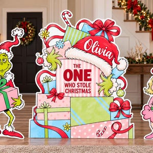 May include: A decorative yard sign set featuring a green character in a red hat holding a pink gift, a stack of colorful gift boxes with the text The One Who Stole Christmas and the name Olivia, and a blonde character in a pink dress holding a gift.