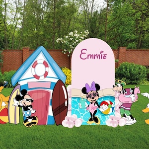 May include: A decorative party display featuring a blue and white beach hut, a pink arch backdrop with the name Emmie, and cutouts of Mickey Mouse, Minnie Mouse, Pluto, Goofy, and Daisy Duck. The scene includes surfboards, a beach ball, and pool.