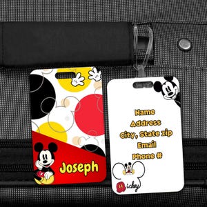 Op de afbeelding: Twee rechthoekige bagagelabels met Mickey Mouse-ontwerpen. E&eacute;n label heeft een rood, geel en zwart kleurenschema met de naam "Joseph". Het andere label is wit met contactgegevens en een Mickey Mouse-afbeelding.