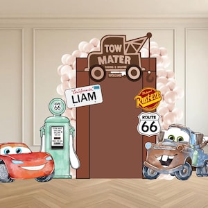 May include: A themed party backdrop featuring cartoon car characters. Includes a red race car, a tow truck, and a gas pump. The backdrop has a brown door with a sign that says "Liam". The Route 66 sign is also visible.