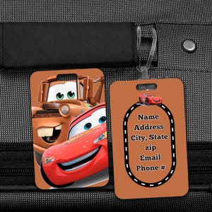 May include: Two luggage tags featuring characters from the animated movie "Cars." One tag displays Lightning McQueen and Mater. The other tag is orange with a race track design and text fields for contact information.