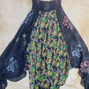 May include: A flowy skirt featuring a smocked elastic waistband and a tiered design. The central panel displays a vibrant floral pattern with green, pink, and blue flowers on a black background, while the side panels feature a darker floral print.