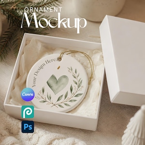 May include: A round white ceramic ornament with a gold hanging string, displayed inside an open white gift box. The ornament features a printed watercolor design of a green heart surrounded by a leafy branch wreath and the text Your Design Here.