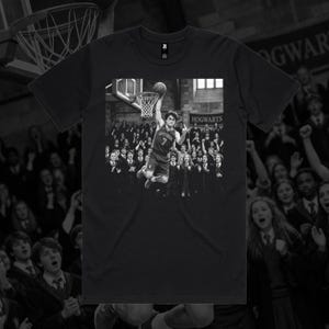 May include: Black t-shirt featuring a black and white image of a basketball player dunking a ball. The image is set in a Hogwarts-themed setting, with the word "Hogwarts" visible. The player is wearing a jersey with the number 7.