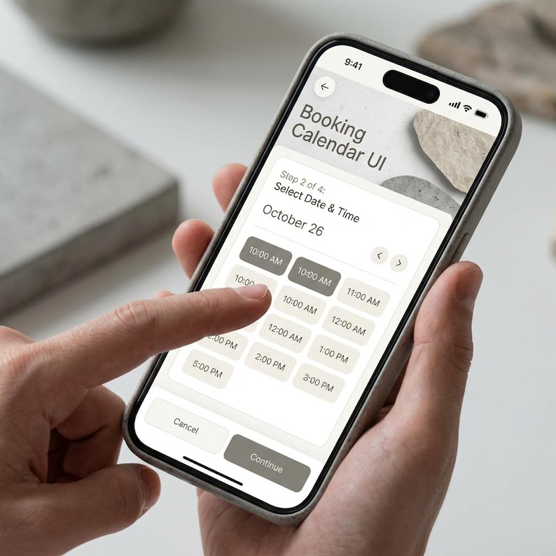 May include: A smartphone displaying a booking calendar UI interface. The screen shows a date selection for October 26th, with time slots from 10:00 AM to 3:00 PM. The phone is held in a gray case, and a finger is touching the screen.