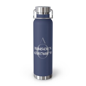May include: A navy blue insulated water bottle with a silver lid and handle. The bottle features white text with the coordinates 18.045436°N 63.017608°W and a stylized design. The bottle is designed to keep beverages cold or hot.