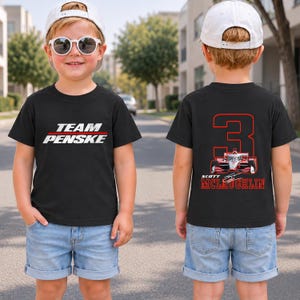 Puede incluir: Una camiseta negra con el texto blanco TEAM PENSKE en la parte delantera. La parte trasera muestra un gran n&uacute;mero 3 rojo, un gr&aacute;fico de coche de carreras rojo y el texto rojo SCOTT MCLAUGHLIN. La camiseta se combina con pantalones cortos de mezclilla azul claro y una gorra blanca.