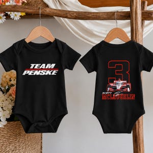 Puede incluir: Dos bodies negros de manga corta para beb&eacute;. El body de la izquierda presenta el texto blanco TEAM PENSKE con una l&iacute;nea roja. El body de la derecha muestra un gran n&uacute;mero 3 rojo, un gr&aacute;fico de coche de carreras rojo y blanco y el texto rojo SCOTT MCLAUGHLIN.