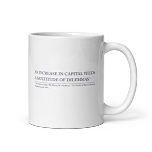 May include: White ceramic mug with a curved handle. The mug features the text "AN INCREASE IN CAPITAL YIELDS A MULTITUDE OF DILEMMAS." in a dark gray font. Below the text is a citation.