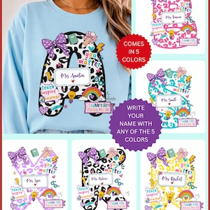 May include: A light blue sweatshirt featuring a large letter A with a black and white leopard print pattern. The letter is decorated with colourful icons including a purple bow, a rainbow, a lightbulb, and text reading you matter, teach inspire courage, and thank you for all you do.