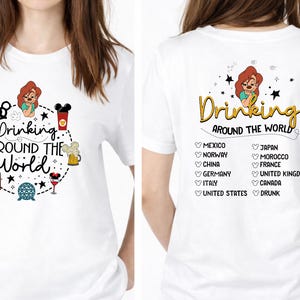 May include: White t-shirt with a colorful graphic design. The front features the text "Drinking Around the World" with cartoon illustrations of drinks. The back of the shirt lists various countries and the word "Drunk".