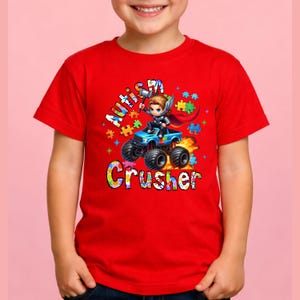Puede incluir: Camiseta roja con un gr&aacute;fico colorido de un superh&eacute;roe conduciendo un cami&oacute;n monstruo azul. El texto de la camiseta dice "Autism Crusher" con acentos de piezas de rompecabezas. El dise&ntilde;o es vibrante y llamativo.