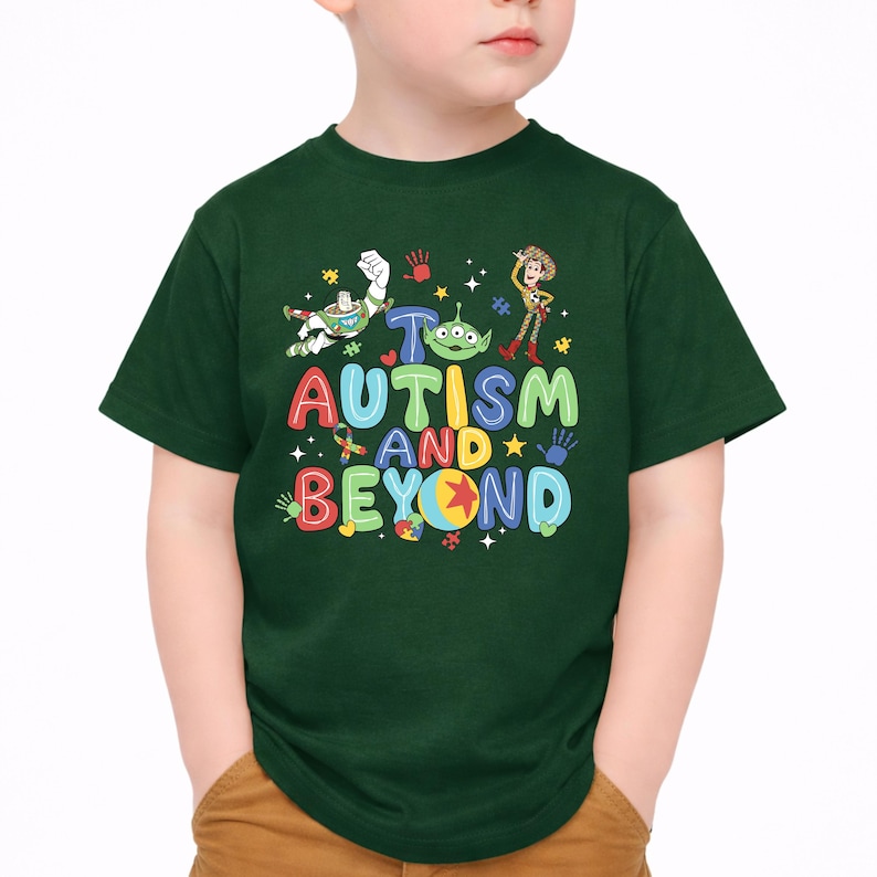 Op de afbeelding: Een donkergroen t-shirt met de tekst "Autism and Beyond" in kleurrijke, speelse letters. Het ontwerp bevat stripfiguren en symbolen die verband houden met autismebewustzijn. Het t-shirt wordt door een kind gedragen.