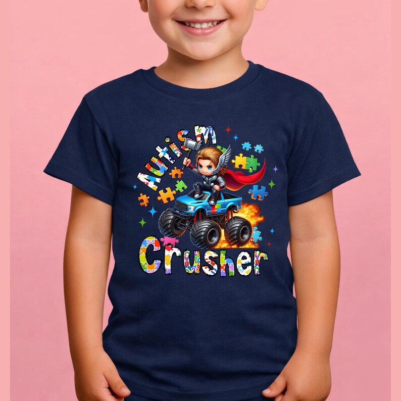 Puede incluir: Camiseta azul marino con un gr&aacute;fico colorido de un superh&eacute;roe conduciendo un cami&oacute;n monstruo. El texto de la camiseta dice "Autism Crusher" con acentos de piezas de rompecabezas. El dise&ntilde;o incluye llamas y estrellas.