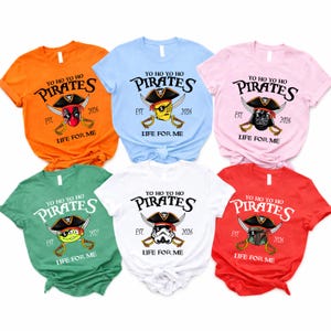 K&ouml;nnte beinhalten: Sechs kurz&auml;rmelige T-Shirts in verschiedenen Farben, jedes mit einem Piraten-Motiv. Die Shirts zeigen den Text "YO HO HO PIRATES" mit verschiedenen Charakterillustrationen, das Jahr "2026" oder "2022" und den Satz "LIFE FOR ME".