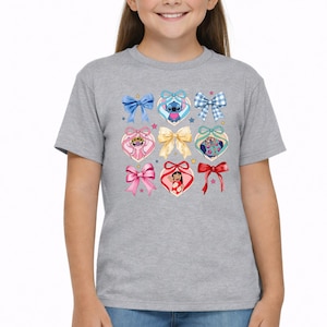 May include: A heather gray t-shirt featuring a central graphic print of various colorful bows and heart-shaped frames. The design includes illustrations of Stitch, Angel, and Lilo from Lilo and Stitch, interspersed with small stars and ribbons.