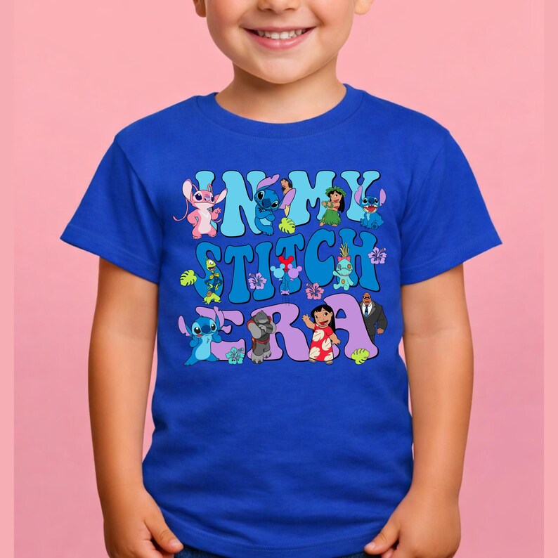 Pode incluir: Uma t-shirt de manga curta azul-real com uma impress&atilde;o gr&aacute;fica com o texto IN MY STITCH ERA. O design inclui v&aacute;rias personagens de desenhos animados coloridas, flores tropicais e folhas verdes dispostas em torno das letras azul-claras.
