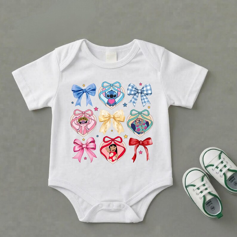 May include: A white short-sleeved baby bodysuit featuring a central graphic print of various colorful bows and heart-shaped frames containing cartoon characters. The design includes blue, pink, red, and yellow bows alongside small star accents.