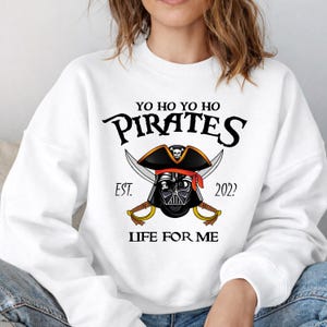 K&ouml;nnte beinhalten: Eine wei&szlig;e Keramiktasse mit schwarzem Henkel und dem Text "But First, Coffee" in handschriftlichem Stil. Die Tasse steht auf einer wei&szlig;en Oberfl&auml;che. Die Tasse ist etwa 10 cm hoch.