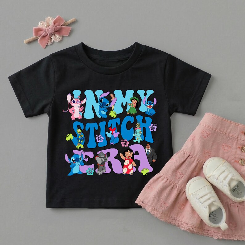 Pode incluir: Uma t-shirt preta de manga curta com uma impress&atilde;o gr&aacute;fica contendo o texto "IN MY STITCH ERA" em letras azuis e roxas, rodeado por v&aacute;rias personagens da franquia Lilo e Stitch, incluindo Stitch, Angel e Lilo.