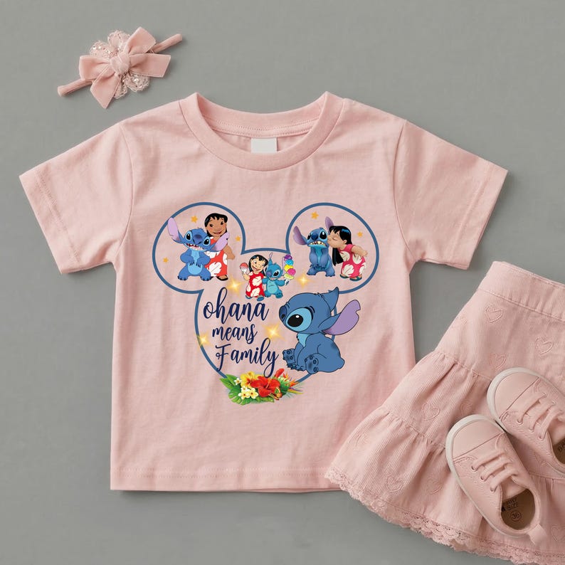 May include: A light pink short-sleeve t-shirt featuring a Mickey Mouse-shaped graphic with Lilo and Stitch characters, the text "Ohana means Family," and tropical flowers. Included are a matching pink hair bow and a tiered pink skirt.