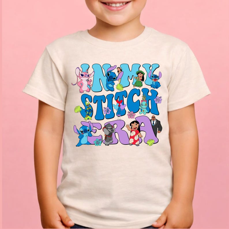 Pode incluir: Uma t-shirt de manga curta na cor creme com uma estampa gr&aacute;fica contendo o texto IN MY STITCH ERA em letras grandes azuis e roxas. O design inclui v&aacute;rios personagens de desenhos animados da franquia Lilo e Stitch e flores tropicais.