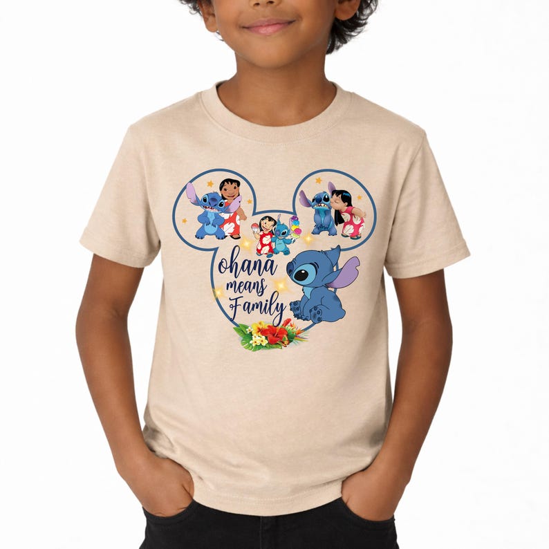 May include: A beige short-sleeve t-shirt featuring a graphic of Stitch and Lilo inside a Mickey Mouse ear outline. The design includes the text Ohana means Family, small yellow stars, and a cluster of tropical hibiscus flowers at the bottom.